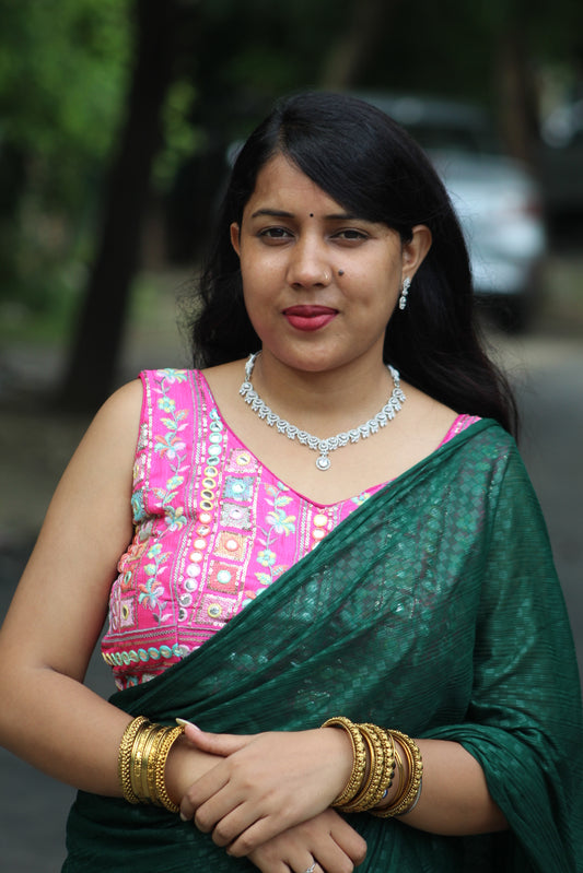 Woman in traditional green and pink saree with jewelry against a blurred natural background