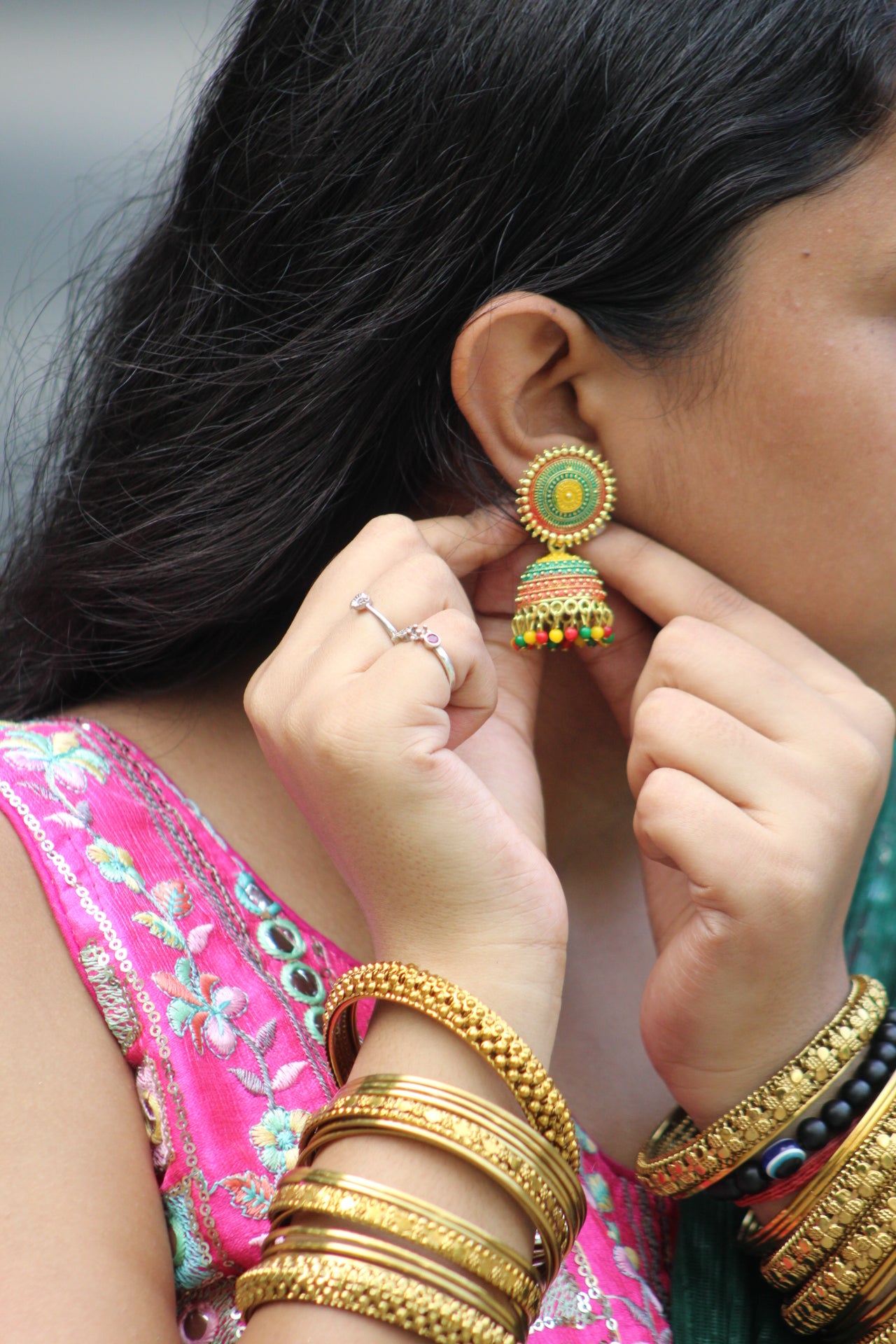 Person wearing gold bangles and a ring, adjusting colorful earrings.